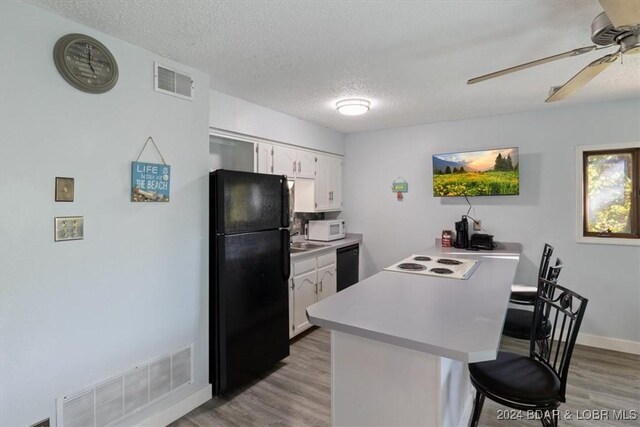 kitchen with kitchen peninsula, a kitchen bar, white cabinetry, and black appliances