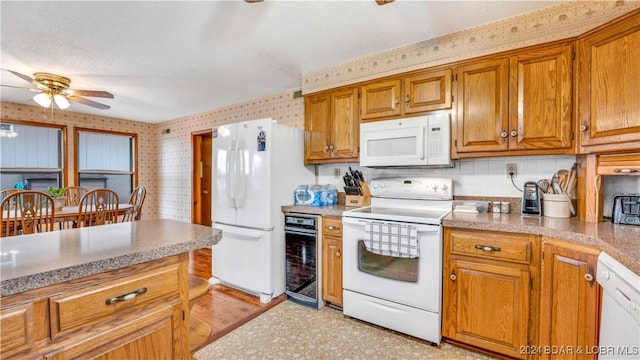 kitchen with wine cooler, brown cabinetry, a ceiling fan, white appliances, and wallpapered walls