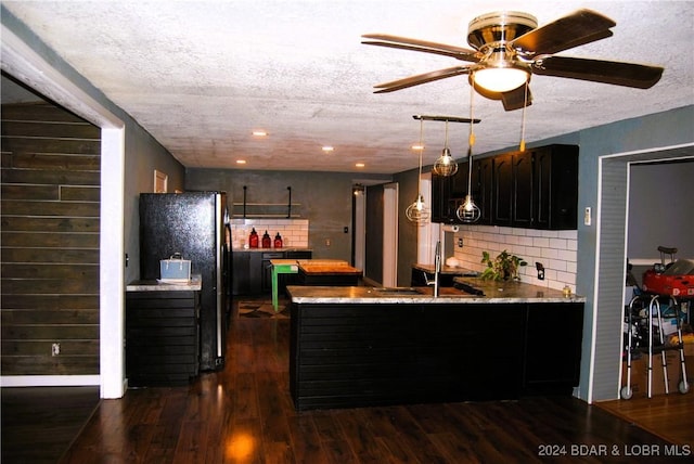 kitchen featuring dark hardwood / wood-style floors, black refrigerator, kitchen peninsula, and backsplash