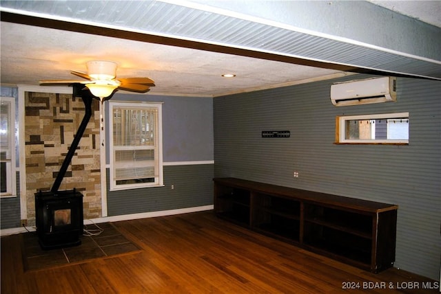 unfurnished living room featuring a wood stove, ceiling fan, dark hardwood / wood-style flooring, a wall unit AC, and crown molding