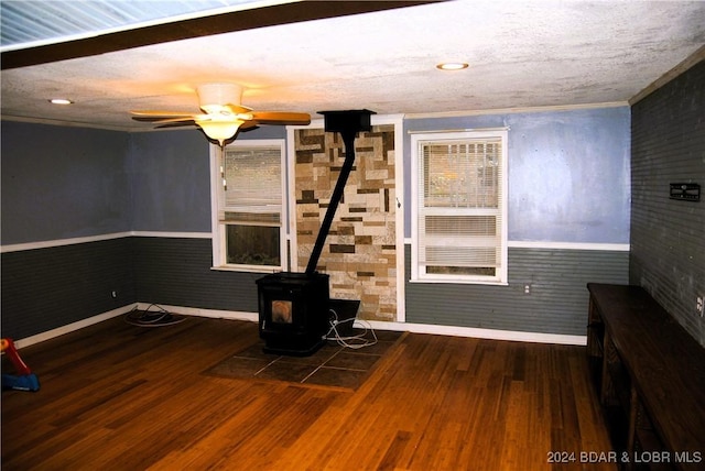 unfurnished living room featuring dark hardwood / wood-style floors, ceiling fan, a wood stove, and crown molding