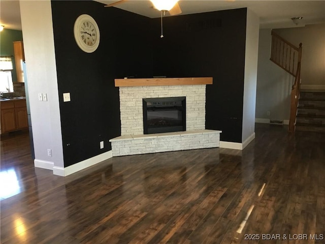 unfurnished living room featuring a brick fireplace, ceiling fan, and dark wood-type flooring