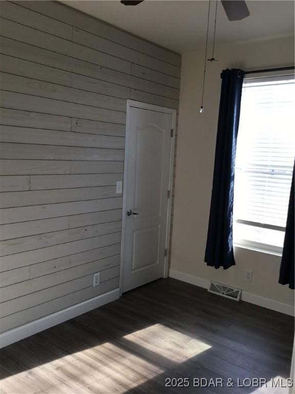 unfurnished room featuring dark hardwood / wood-style floors, wood walls, and ceiling fan