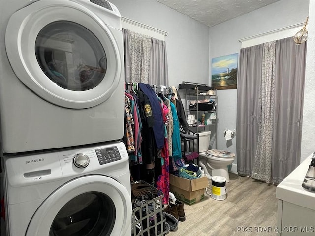 clothes washing area featuring light hardwood / wood-style floors, stacked washer / dryer, and a textured ceiling