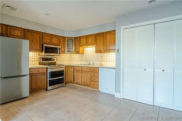 kitchen featuring backsplash, sink, light tile patterned floors, and stainless steel appliances