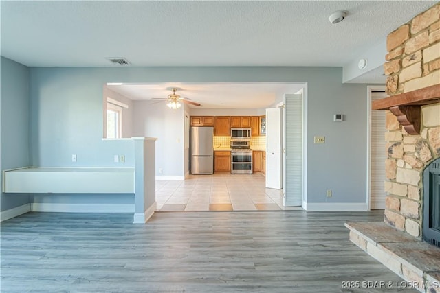 unfurnished living room with a stone fireplace, ceiling fan, light hardwood / wood-style flooring, and a textured ceiling