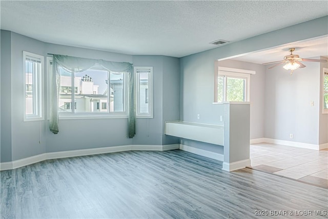 empty room with ceiling fan, light wood-type flooring, and a textured ceiling