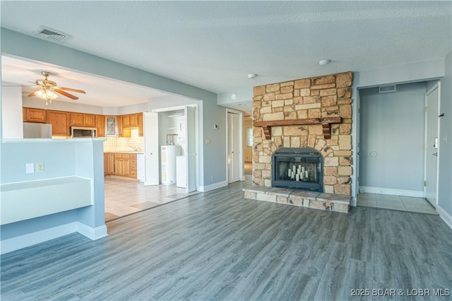 unfurnished living room featuring a fireplace, wood-type flooring, a textured ceiling, and ceiling fan