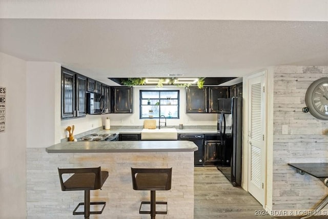 kitchen with a breakfast bar area, kitchen peninsula, sink, and black appliances