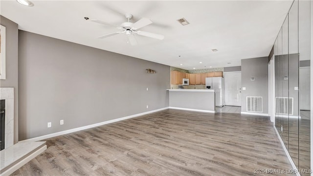 unfurnished living room featuring a tile fireplace, light wood-type flooring, and ceiling fan