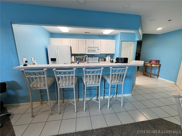 kitchen with kitchen peninsula, a breakfast bar, white appliances, light tile patterned floors, and white cabinets