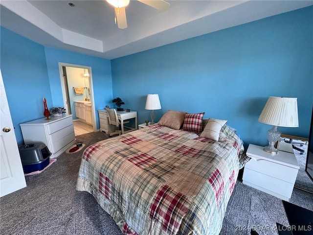 carpeted bedroom featuring a tray ceiling, ceiling fan, and ensuite bathroom