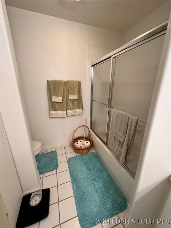 bathroom featuring tile patterned floors, toilet, and bath / shower combo with glass door