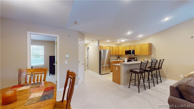 kitchen with kitchen peninsula, appliances with stainless steel finishes, a breakfast bar, light colored carpet, and light brown cabinets