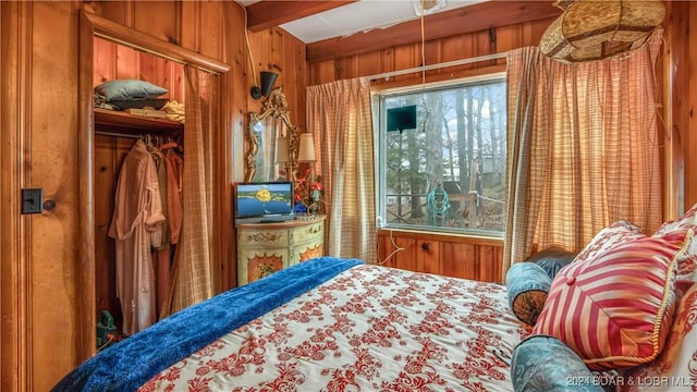 bedroom featuring wood walls, beam ceiling, and a closet