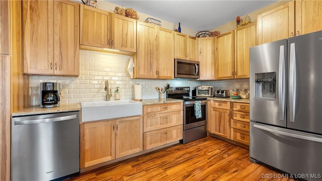 kitchen featuring hardwood / wood-style floors, sink, tasteful backsplash, light stone counters, and stainless steel appliances