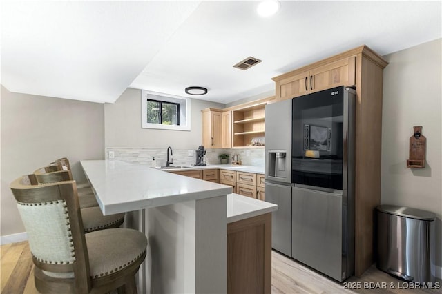 kitchen featuring sink, a breakfast bar, tasteful backsplash, kitchen peninsula, and light brown cabinets