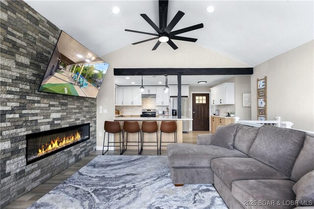 living room featuring ceiling fan, dark hardwood / wood-style floors, a stone fireplace, and lofted ceiling