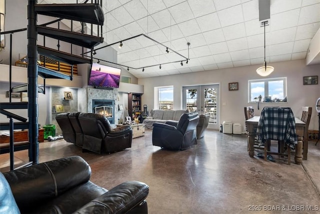 living room featuring finished concrete flooring, french doors, a glass covered fireplace, and track lighting