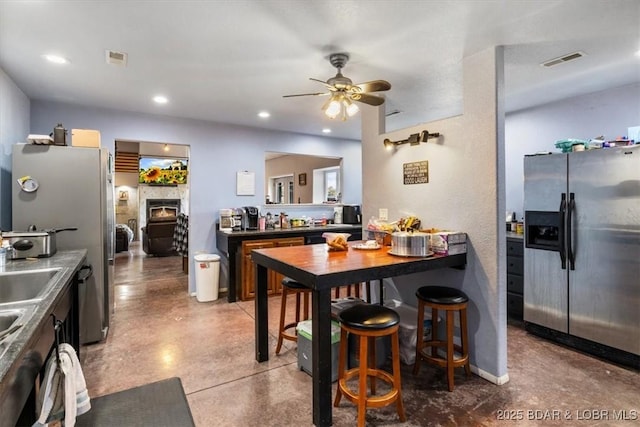 kitchen featuring visible vents, a lit fireplace, concrete floors, stainless steel refrigerator with ice dispenser, and recessed lighting