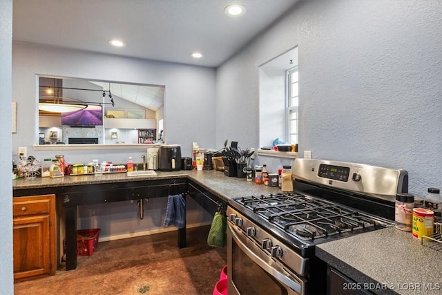 kitchen with brown cabinets, lofted ceiling, dark countertops, a textured wall, and stainless steel gas range oven