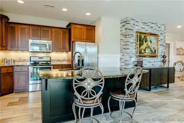 kitchen with stone counters, sink, an island with sink, appliances with stainless steel finishes, and tasteful backsplash