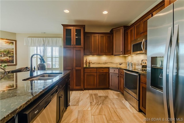 kitchen with dark stone countertops, decorative backsplash, sink, and appliances with stainless steel finishes