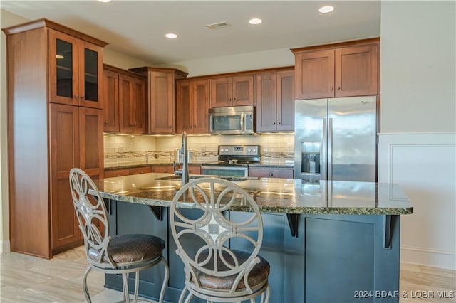 kitchen featuring appliances with stainless steel finishes, dark stone counters, a center island with sink, and a breakfast bar area