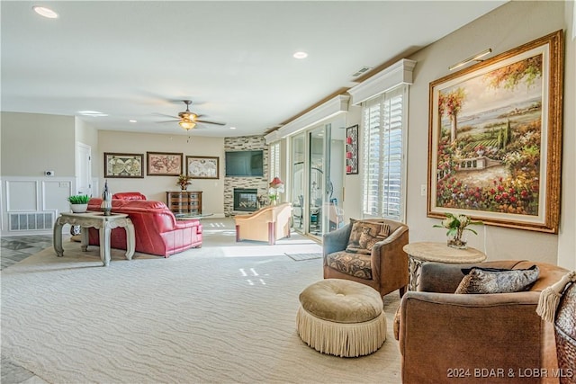 living room featuring a large fireplace, light colored carpet, and ceiling fan