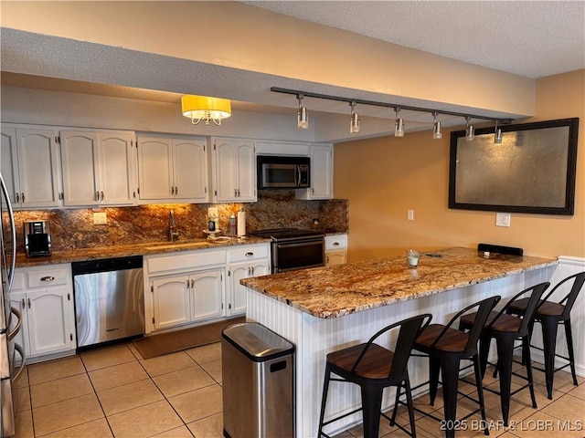 kitchen with stone countertops, appliances with stainless steel finishes, a breakfast bar area, a peninsula, and light tile patterned flooring