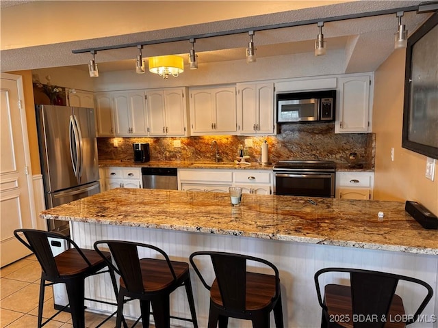 kitchen with light stone counters, light tile patterned floors, stainless steel appliances, decorative backsplash, and a sink