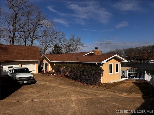 view of front of house featuring driveway, a chimney, an attached garage, and roof with shingles