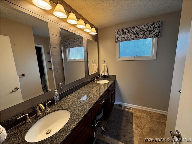 bathroom featuring a textured ceiling, a sink, visible vents, baseboards, and double vanity