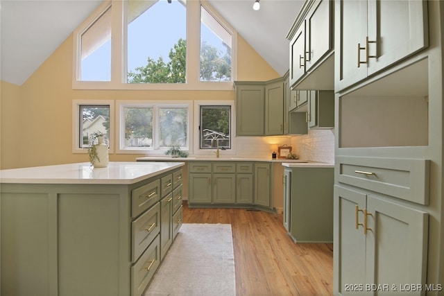 kitchen with tasteful backsplash, high vaulted ceiling, light hardwood / wood-style flooring, green cabinetry, and a kitchen island