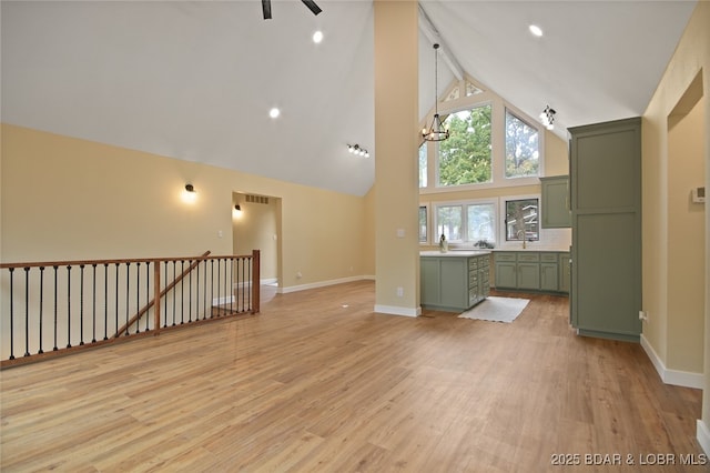 unfurnished living room featuring light hardwood / wood-style flooring, high vaulted ceiling, a notable chandelier, and sink