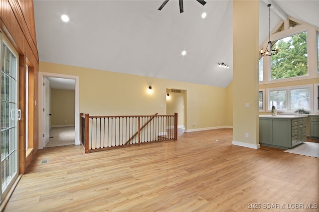 unfurnished living room featuring beam ceiling, light hardwood / wood-style floors, a wealth of natural light, and a notable chandelier