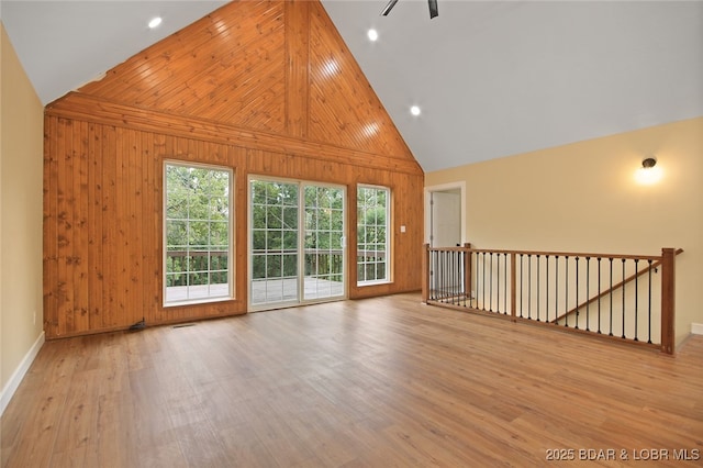 unfurnished living room featuring ceiling fan, high vaulted ceiling, wood walls, and light wood-type flooring