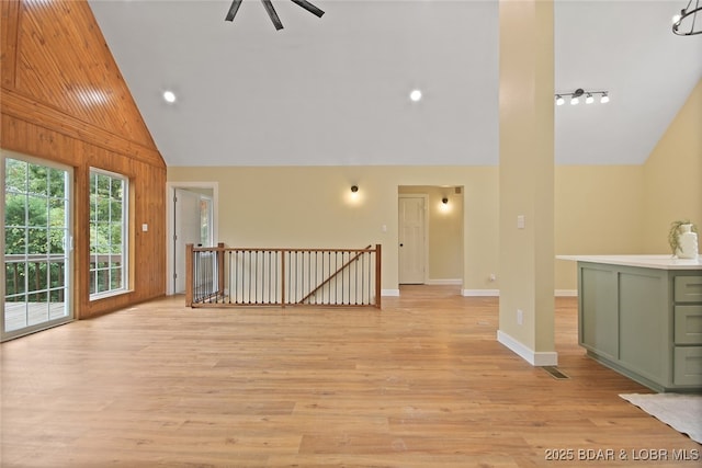 unfurnished living room with ceiling fan, light hardwood / wood-style flooring, high vaulted ceiling, track lighting, and wooden walls