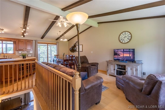 living room featuring ceiling fan with notable chandelier, lofted ceiling with beams, light hardwood / wood-style flooring, and sink