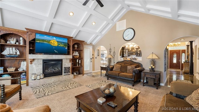 carpeted living room with a high end fireplace, ceiling fan, built in features, a towering ceiling, and beam ceiling