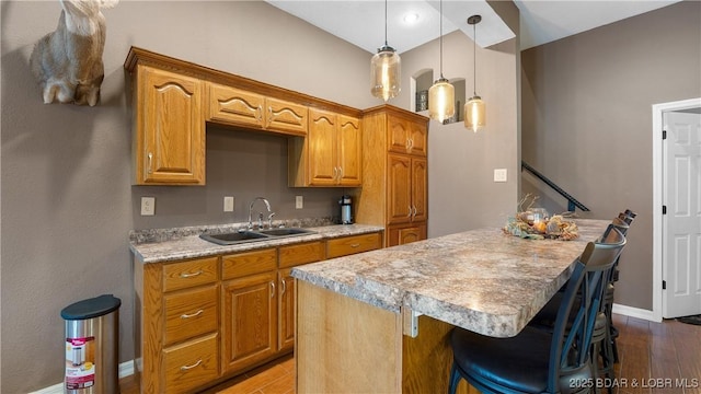 kitchen featuring hardwood / wood-style floors, pendant lighting, sink, a kitchen island, and a kitchen bar