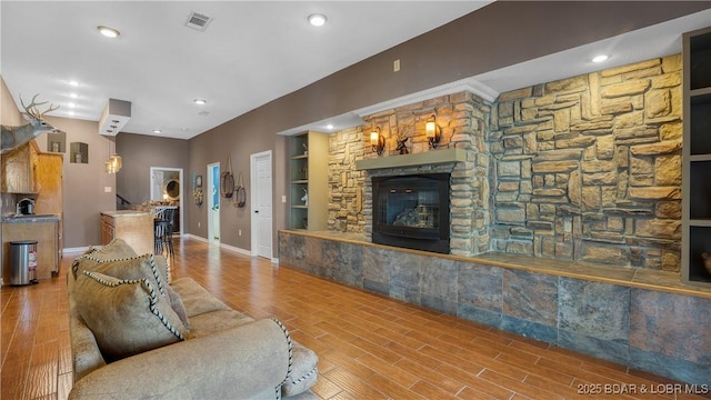 living room featuring hardwood / wood-style flooring, built in shelves, a stone fireplace, and sink