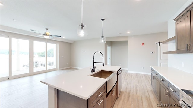 kitchen with light wood-type flooring, stainless steel dishwasher, ceiling fan, a barn door, and a center island with sink