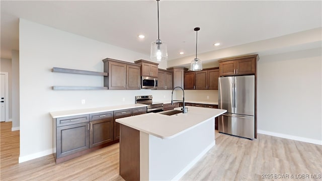 kitchen featuring sink, stainless steel appliances, light hardwood / wood-style flooring, pendant lighting, and a center island with sink