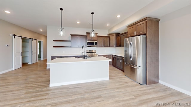 kitchen with sink, a barn door, an island with sink, appliances with stainless steel finishes, and decorative light fixtures