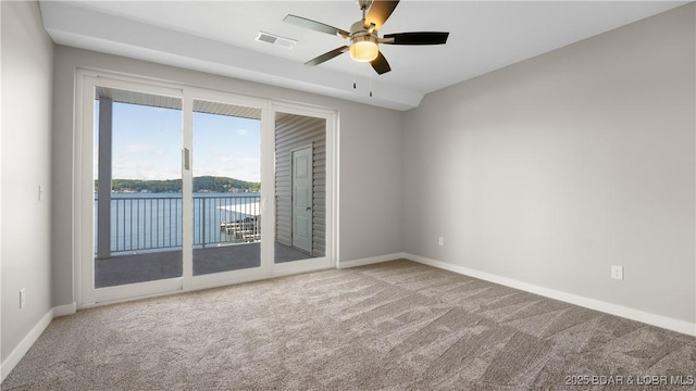 carpeted empty room with a water view and ceiling fan