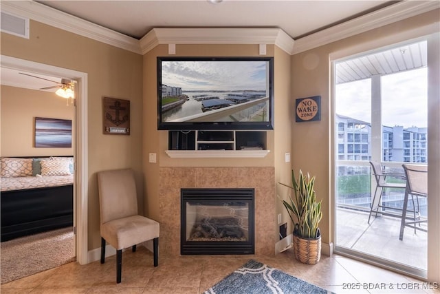 living area with light tile patterned floors, ceiling fan, ornamental molding, and a tiled fireplace