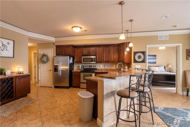 kitchen featuring kitchen peninsula, stainless steel appliances, crown molding, hanging light fixtures, and a breakfast bar area