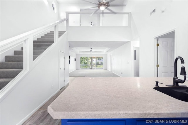 kitchen with sink, blue cabinets, a towering ceiling, light hardwood / wood-style floors, and ceiling fan