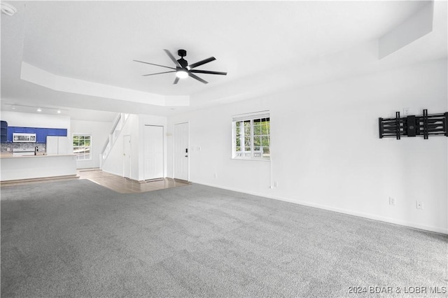 unfurnished living room featuring ceiling fan, a raised ceiling, carpet, and a wealth of natural light